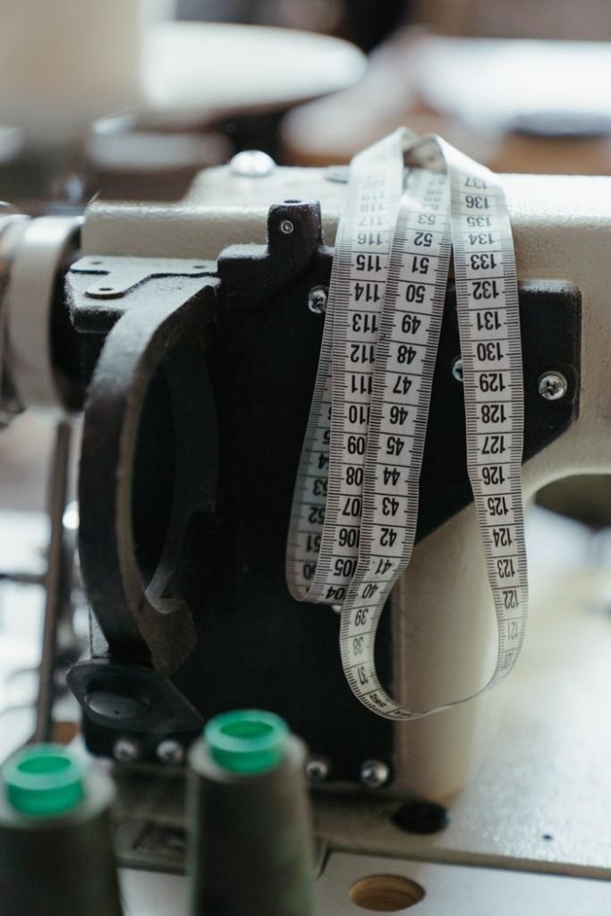 black-and-silver-steel-tool-4614250 Close-up of a sewing machine with measuring tape in a workshop, highlighting tailoring tools.
